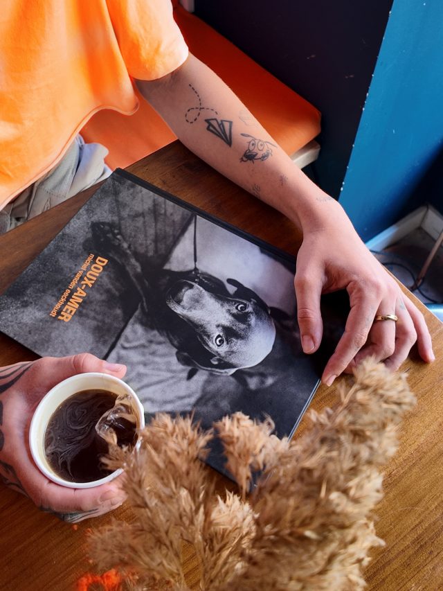 English version ⬇️ 
🇪🇸
 Las portadas también cuentan quiénes somos.
 Sobre la mesa, nuestra revista de Doux - Amer muestra en su portada una fotografía en blanco y negro que nos recuerda a Niki, la perrita que inspira nuestro espíritu dog friendly 🐾🖤
Unas manos están a punto de cogerla mientras sostienen un americano, esa pausa rápida que sabe a calma y rutina bonita.
 En Doux - Amer, cada detalle está pensado para acompañarte.
📍 Doux - Amer / Centro y Cabanyal
#DouxAmer #BrunchVLC #DogFriendlyValencia NikiGirl CafeValencia IcedAmericano CoffeeLovers DouxAmerCafe CoverStory SlowMornings
———————————
🇬🇧
 Covers also tell who we are.
 On the table lies our Doux - Amer magazine featuring on its cover a black-and-white photograph that reminds us of Niki, the little dog behind our dog-friendly soul 🐾🖤
A pair of hands is about to pick it up while holding an  americano ,a quick pause that still feels warm and comforting.
 At Doux - Amer, every detail is meant to be shared.
📍 Doux - Amer / Center and Cabañal
DouxAmer BrunchVLC DogFriendlyValencia NikiGirl IcedAmericano CoffeeLovers DouxAmerCafe CoverStory CozyVibes ValenciaCoffee